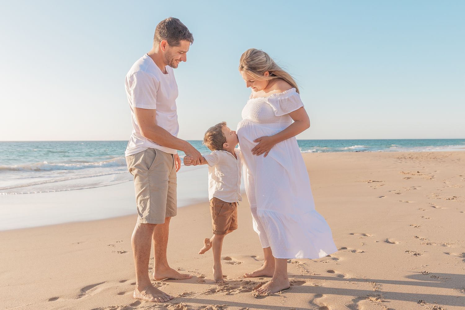 A family shares a tender moment together on a sunny beach with the ocean in the background.