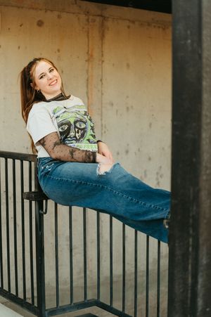 Person in jeans and graphic t-shirt lounges casually on concrete ledge with black metal railing in artistic pose.