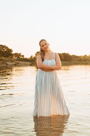 A woman in a striped dress poses gracefully in calm water at sunset creating a serene reflection.
