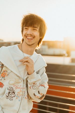 Person wearing white embroidered shirt smiling in warm sunset light on wooden bench.