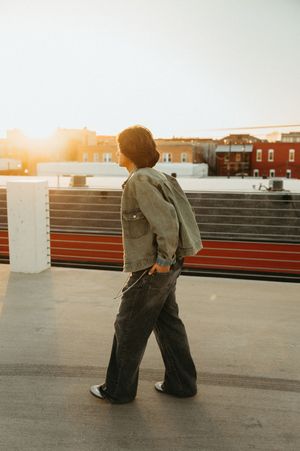 Person in casual clothing kneeling on a rooftop against a warm sunset sky with urban buildings in the background.