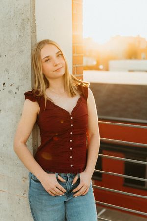 A person in a burgundy button-up top and jeans poses against a concrete wall during golden hour sunset.