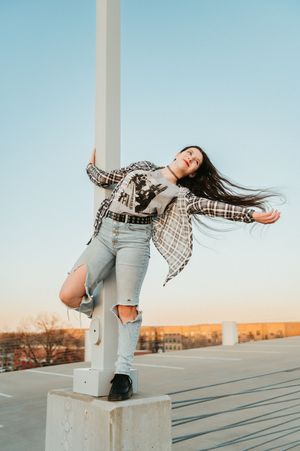 A person in a plaid shirt and jeans dances expressively on a rooftop at sunset.