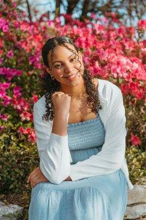 A person in a white dress poses gracefully among tall wildflowers during golden hour sunset.
