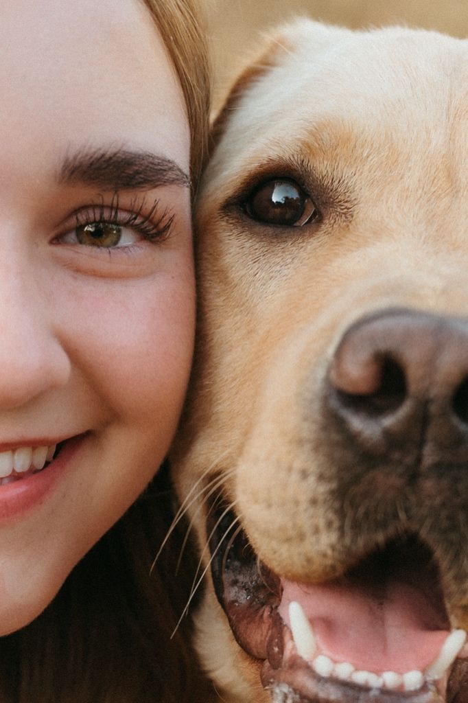 Young woman smiling cheek-to-cheek with a golden Labrador dog in a close-up portrait photo.