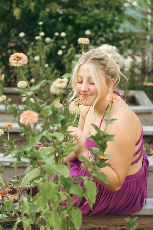 Woman in light blue midi dress with smocked bodice posing in a garden with colorful flowers and stone pathway.