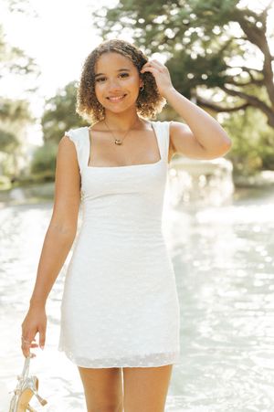 Young woman in a light blue floral sundress poses by a rustic wooden fence in a summer outdoor setting.