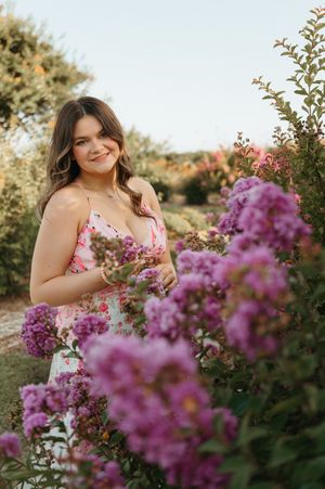 Young woman in a light blue floral sundress poses by a rustic wooden fence in a summer outdoor setting.