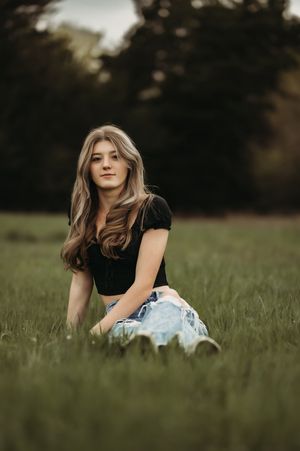 Someone wearing a black crop top and light denim sits casually in a grassy field during golden hour.