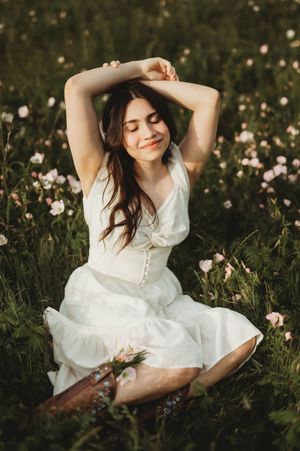 A person in a flowing white dress sits dreamily in a wildflower field at golden hour.