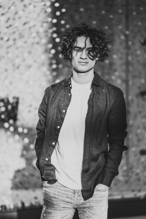 Black and white portrait of person with curly hair wearing denim and leather jacket against sparkly background.