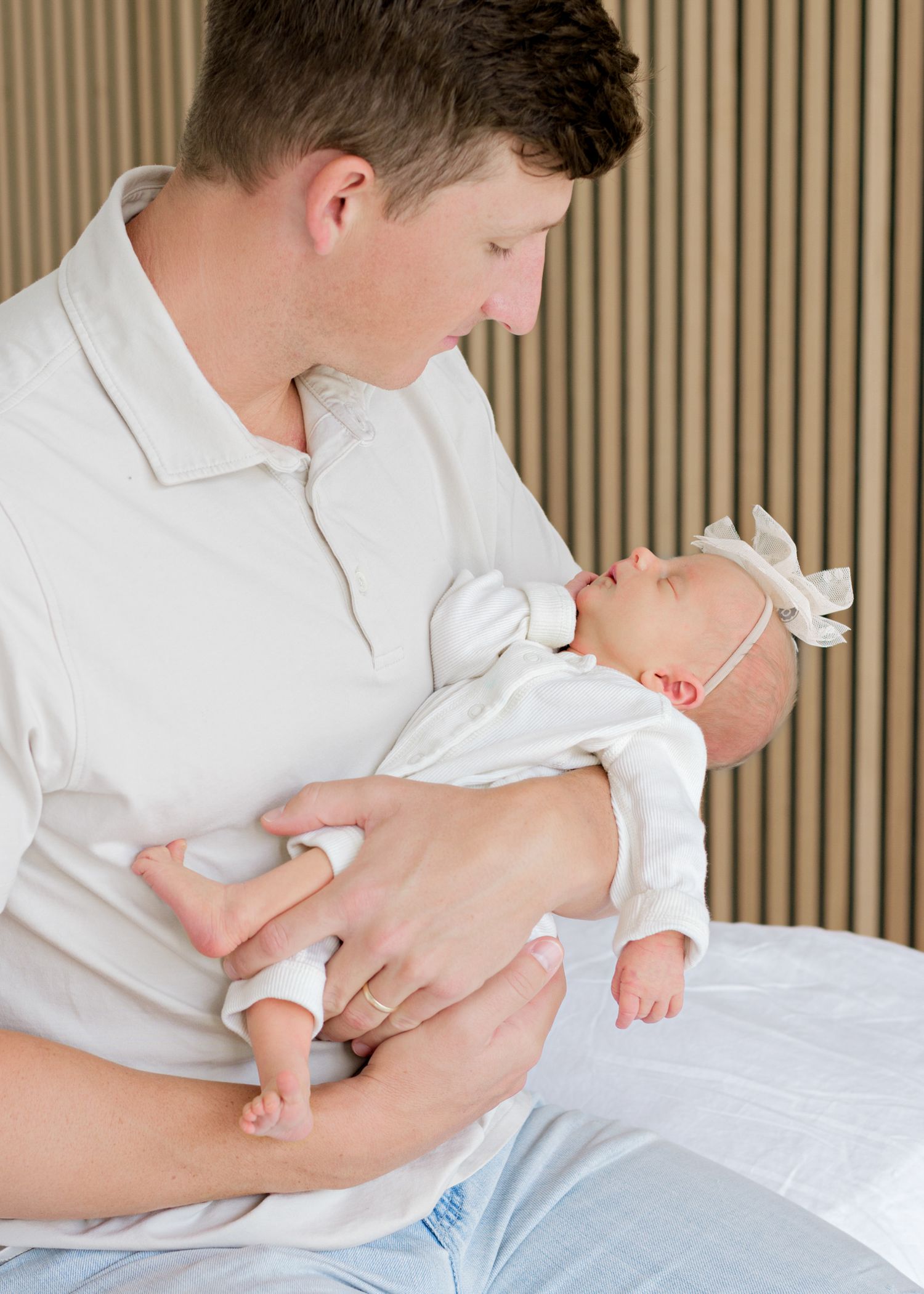 Tender moment as parent in white shirt holds and gazes lovingly at newborn baby swaddled in white.