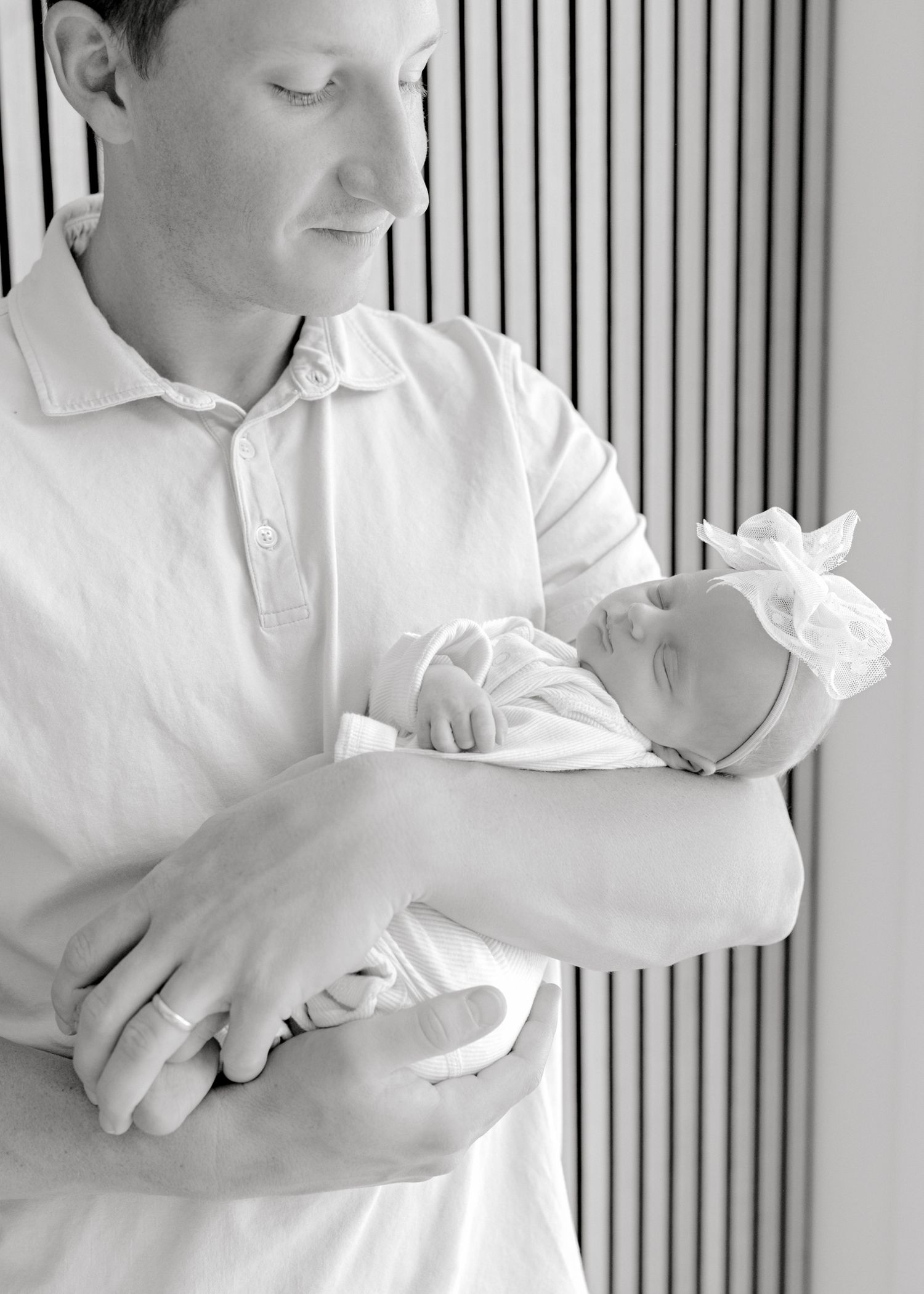 A tender black and white portrait of a parent in a white polo shirt cradling a tiny newborn baby.