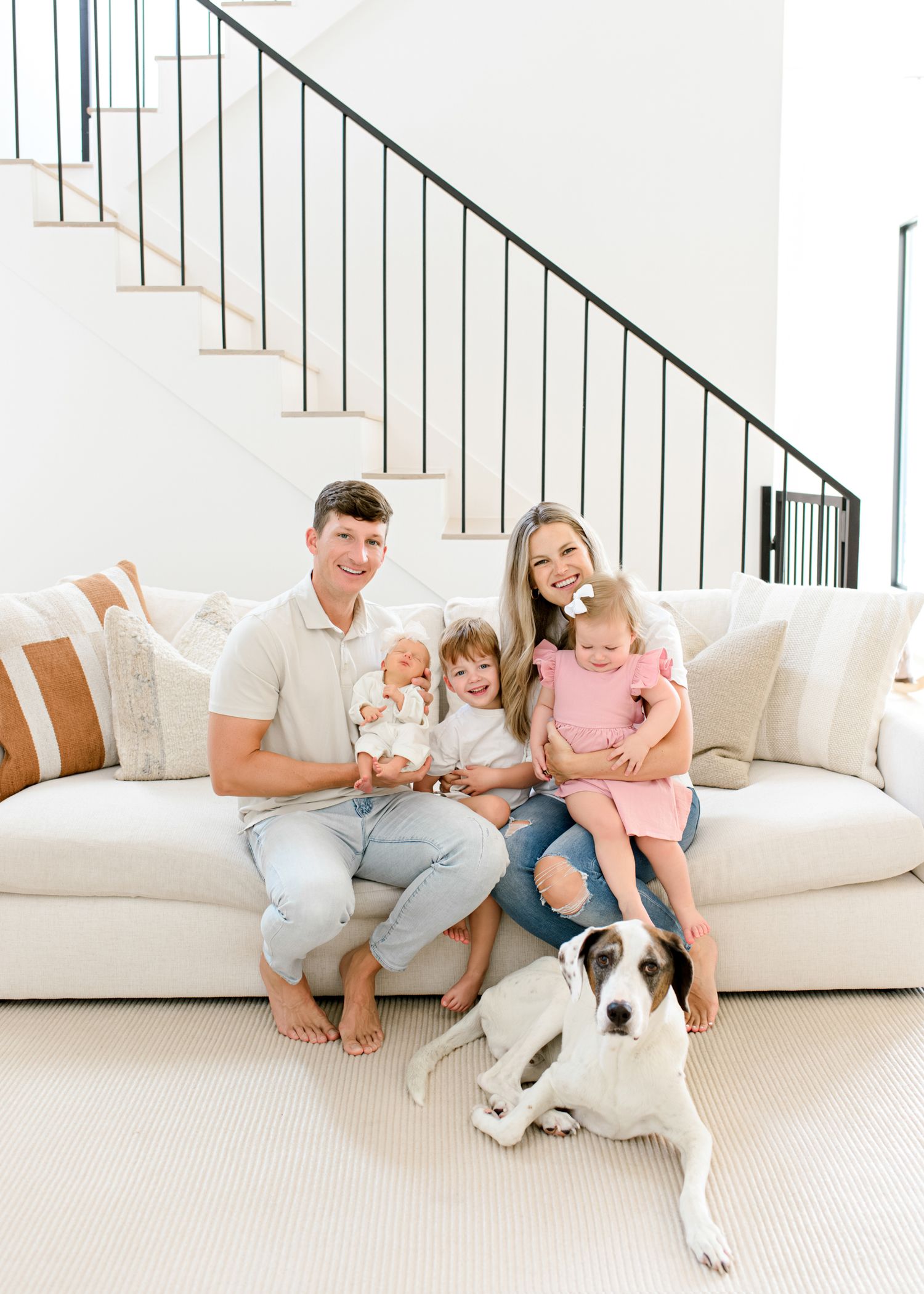 A happy family relaxes on a white couch with their black and white dog in a bright modern living room.