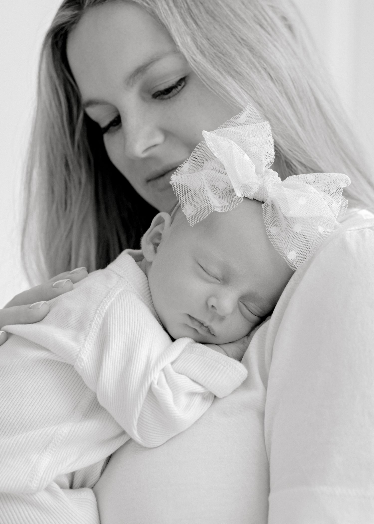 A sleeping baby in white clothing rests against someone in a tender black and white portrait.