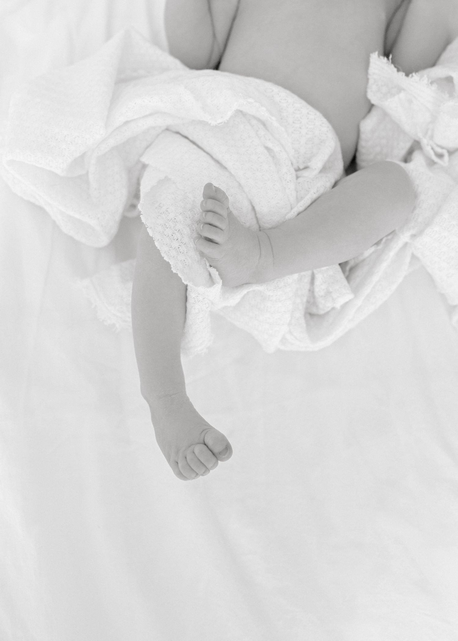 Close-up black and white photograph of a tiny baby foot wrapped in soft white fabric.