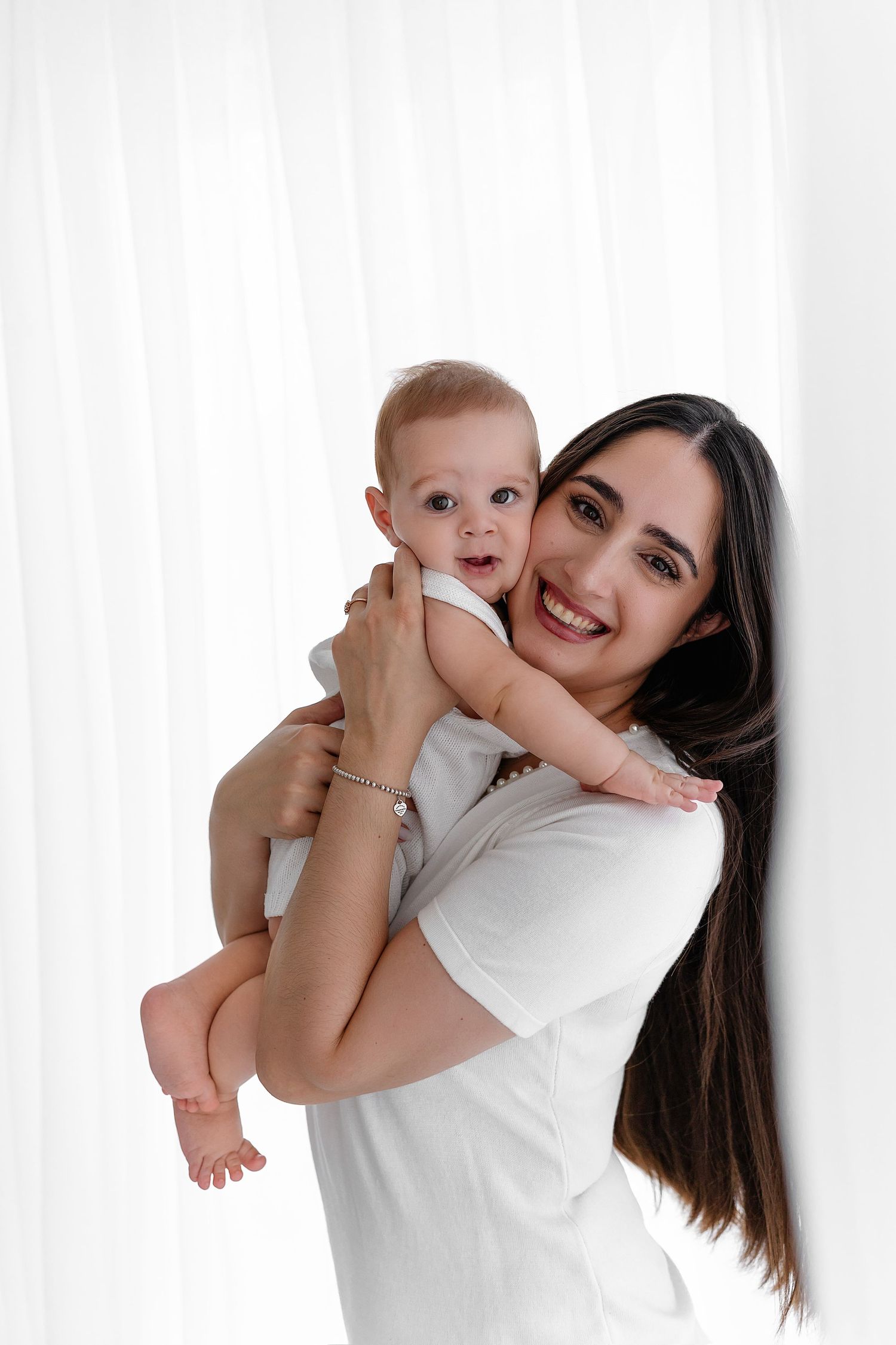 A woman in a white t-shirt holds a happy baby against a white background.