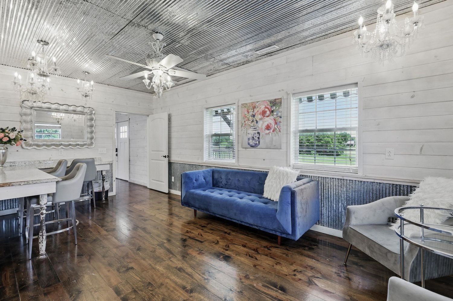 Modern open concept living room with blue velvet sofa, white shiplap walls, hardwood floors and crystal chandeliers.