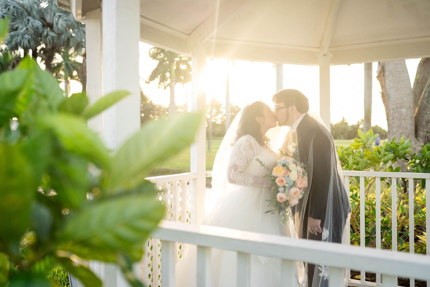 A romantic scene captured at sunset in a white gazebo surrounded by lush greenery and hanging decorative bunting.
