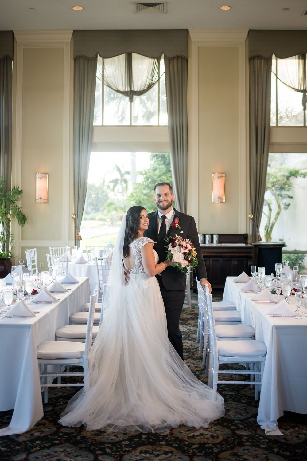 Elegant wedding reception setup with tall windows, wall sconces, and long banquet tables dressed in crisp white linens.