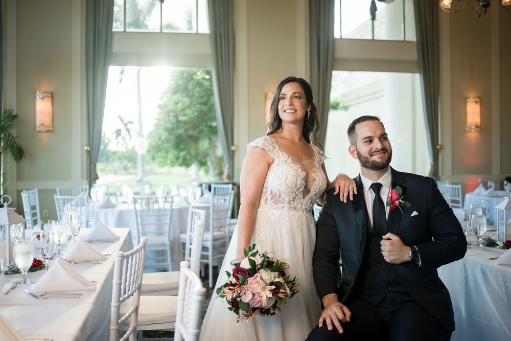 Elegant couple poses in beautifully decorated wedding reception venue with tall windows and soft blue decor.