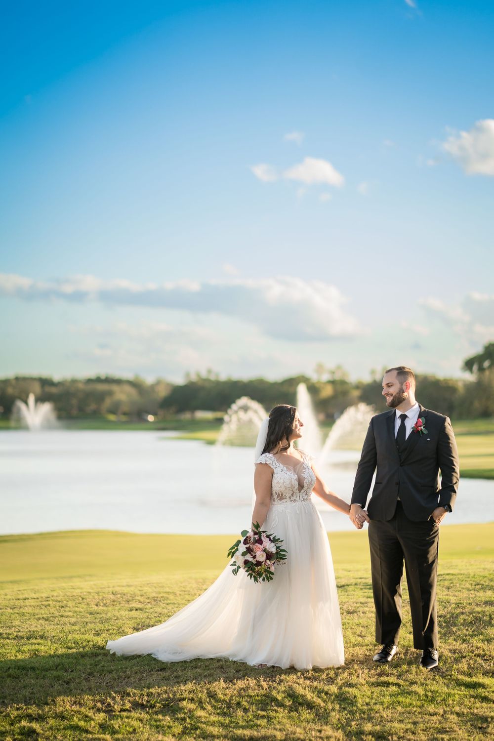 Wedding couple standing on golf course with fountains and lake in background during golden hour.