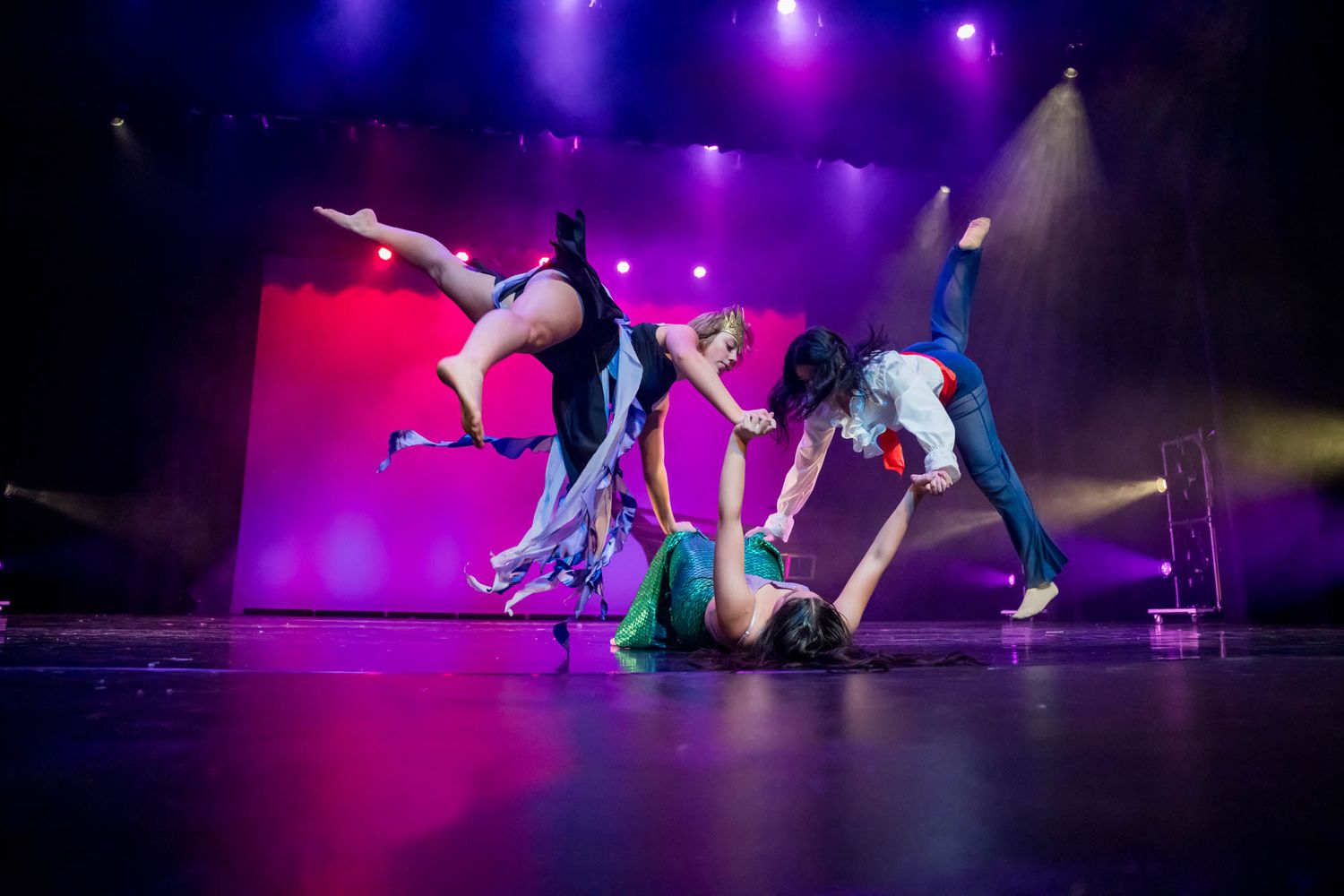 Dancers perform dynamic modern dance moves on stage with dramatic purple and red lighting effects in the background.