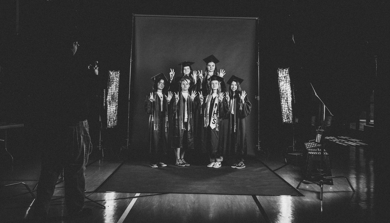 A group of 2025 NPA graduates stand together on a dark stage in graduation-style robes during senior portraits by Sean Openshaw Photography.