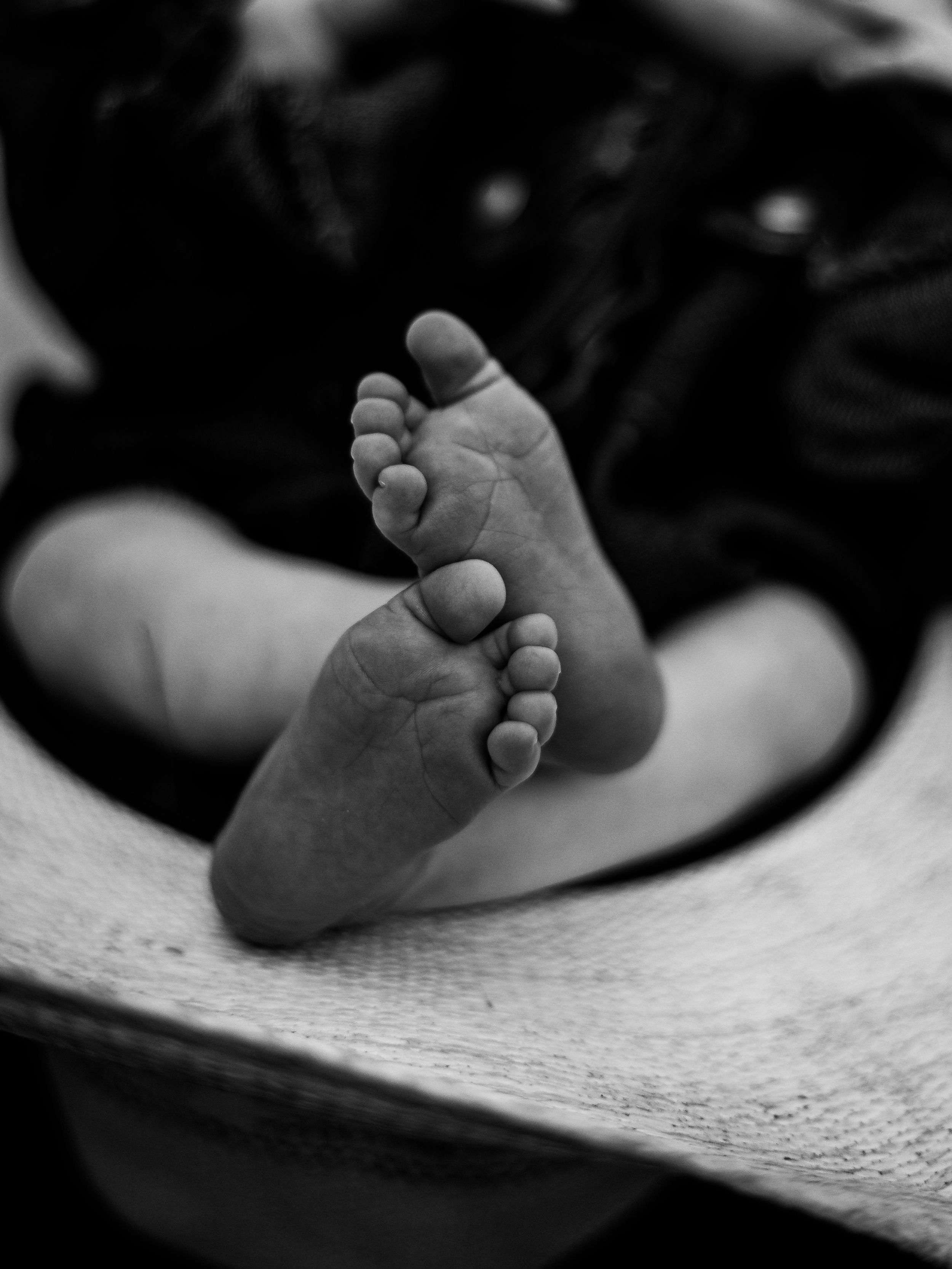 Black and white close-up of tiny baby feet against a textured surface.