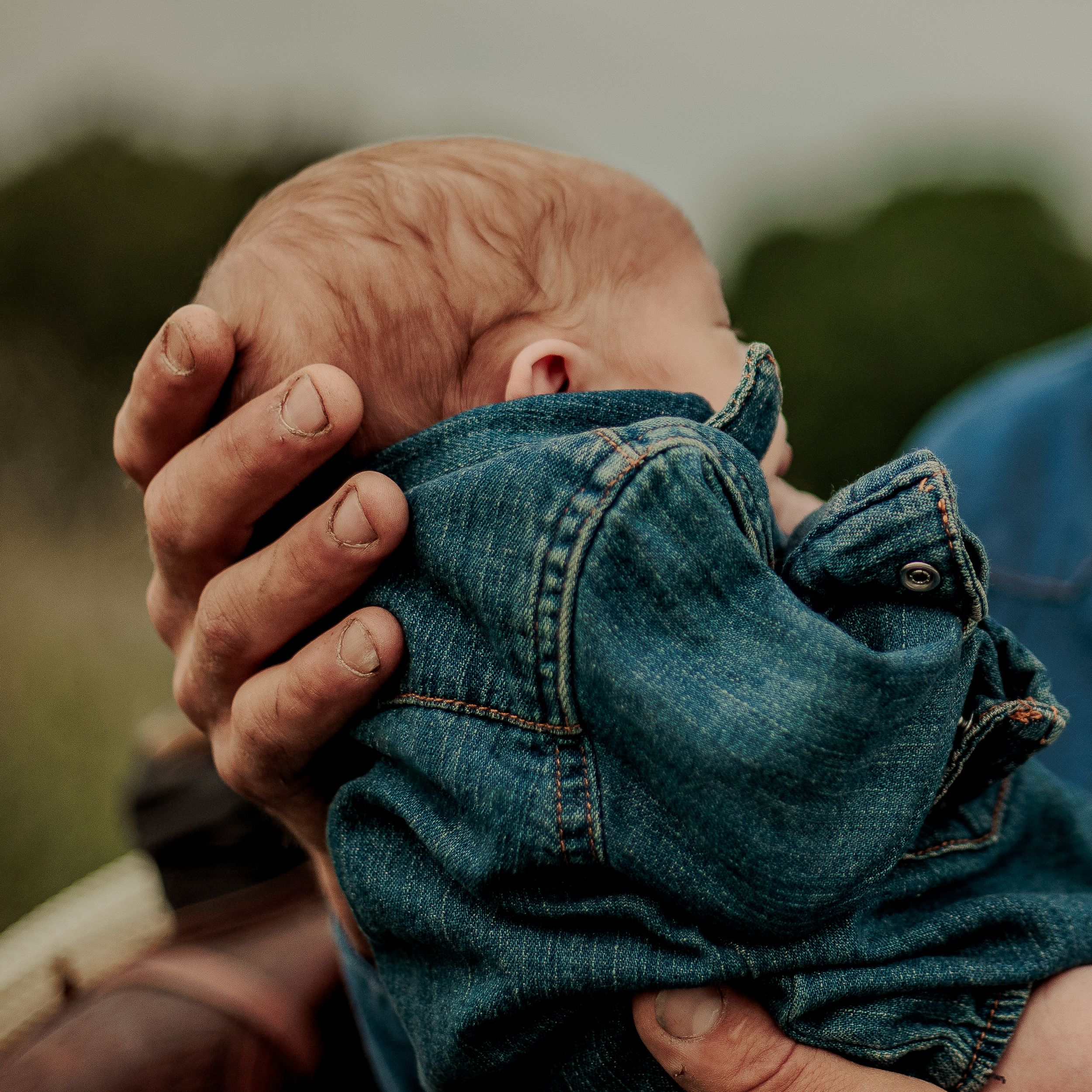 Hands holding and folding blue denim jeans in a sequence of images against a blurred outdoor background.