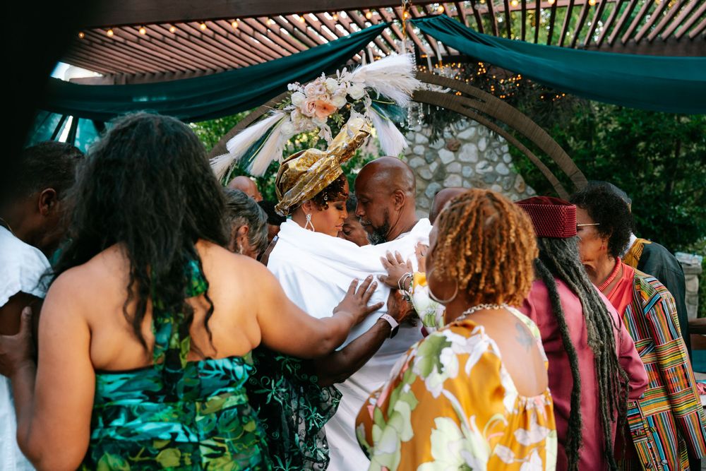 A group of people celebrate at an outdoor party under a teal canopy with wooden slats.