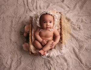 Baby sitting in basket wearing lace bonnet looking up at camera for photoshoot