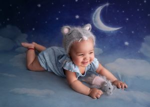 baby laying on stomach wearing rat bonnet holding rat stuffed animal
