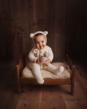 baby sitting on bed in teddy bear outfit