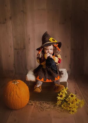 Baby in Halloween costume sitting on chair with pumpkin