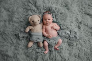 Baby laying on fur holding teddy bear stuffed animal looking at camera
