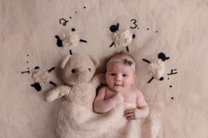baby laying on back holding stuffed animal and blanket