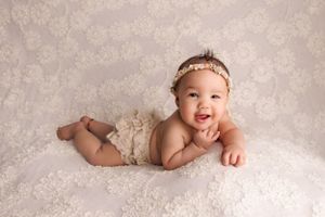 baby laying on tummy smiling at camera with hand in mouth newborn photography