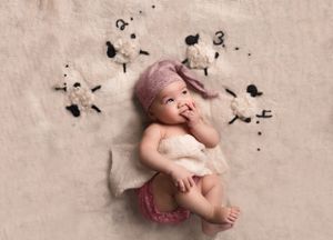 Baby laying on counting sheep backdrop with sleepy cap on