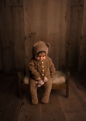 Sitting baby wearing teddy bear outfit holding teddy bear stuffed animal