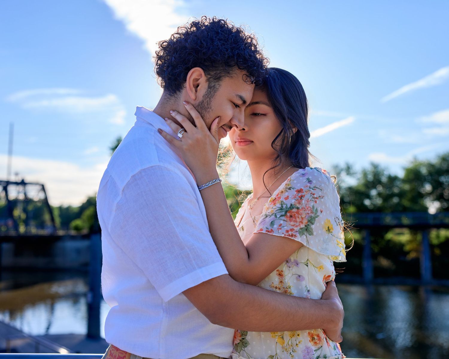 Romantic backlit portrait of a young couple embracing tenderly outdoors, foreheads touching. Intimate engagement photography.