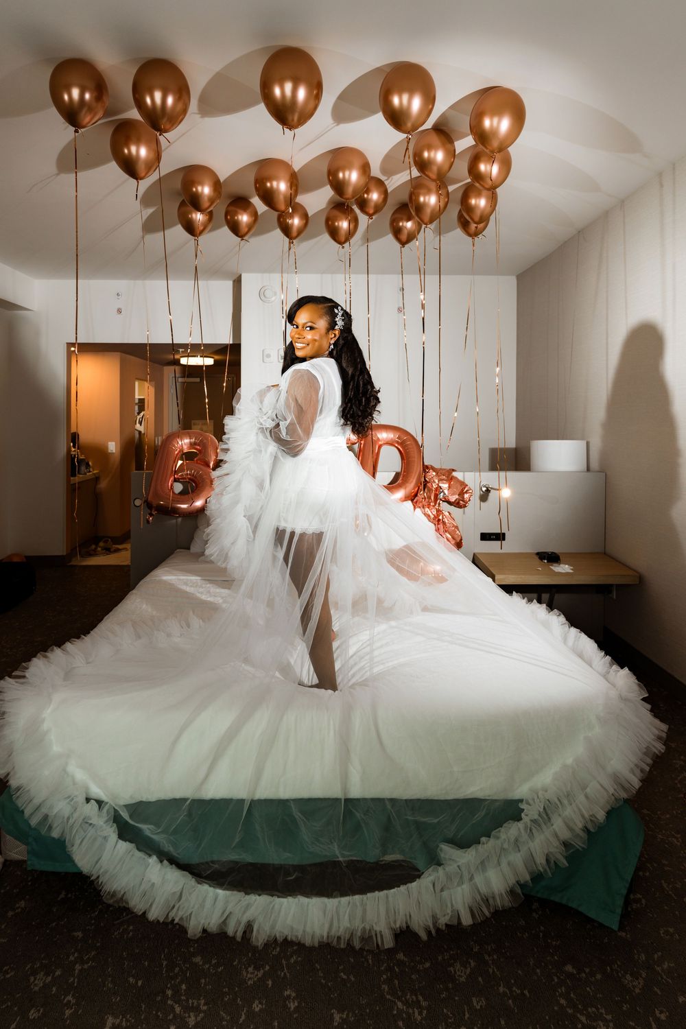 A dramatic bridal photo with a flowing white tulle gown and copper balloons decorating the ceiling in an indoor setting.