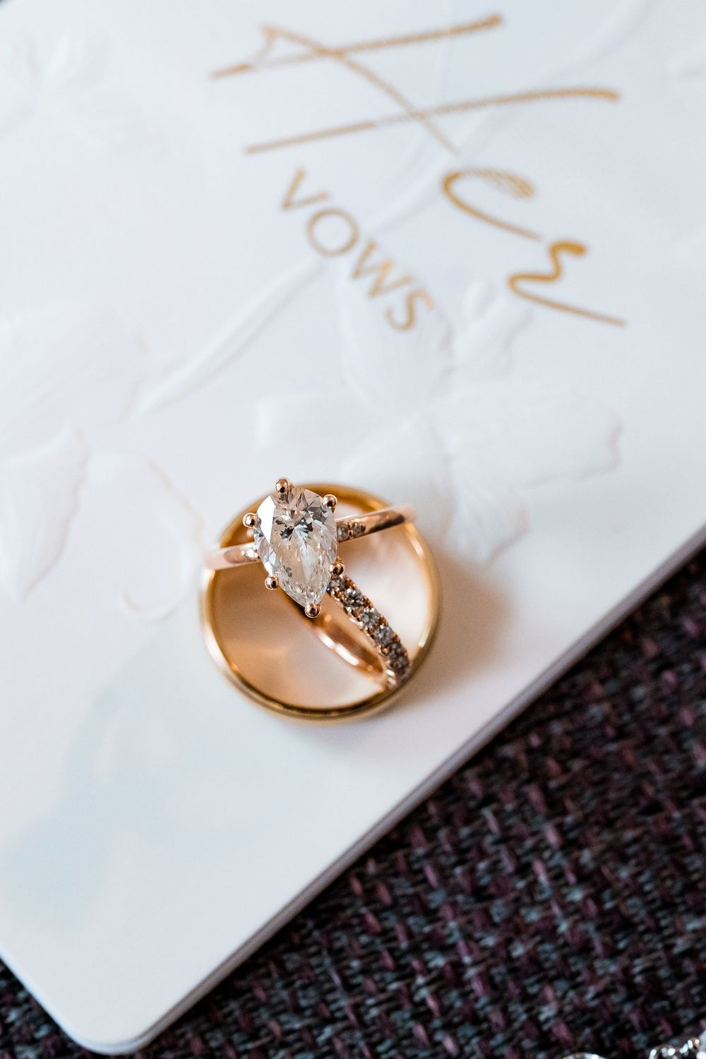 A gold engagement ring with a marquise diamond and split shank design rests on white vow cards.