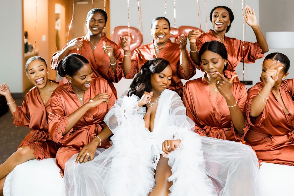 A bridal party wearing matching silk coral robes shares a fun candid moment together before the wedding ceremony.