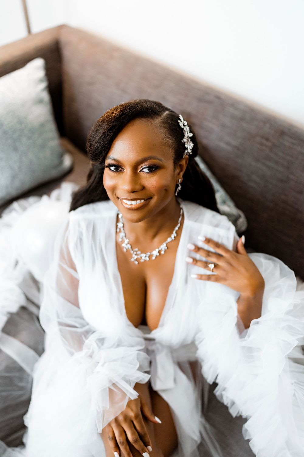 Beautiful wedding portrait featuring a bride in white robe and delicate jewelry sitting on grey couch.