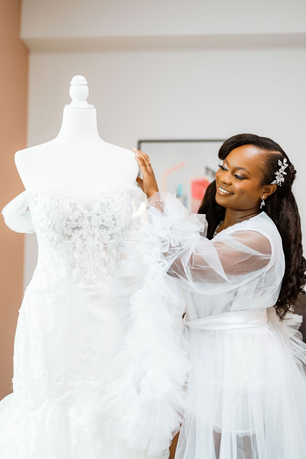 A lacy white wedding gown displayed on mannequin being adjusted in bridal fitting room.