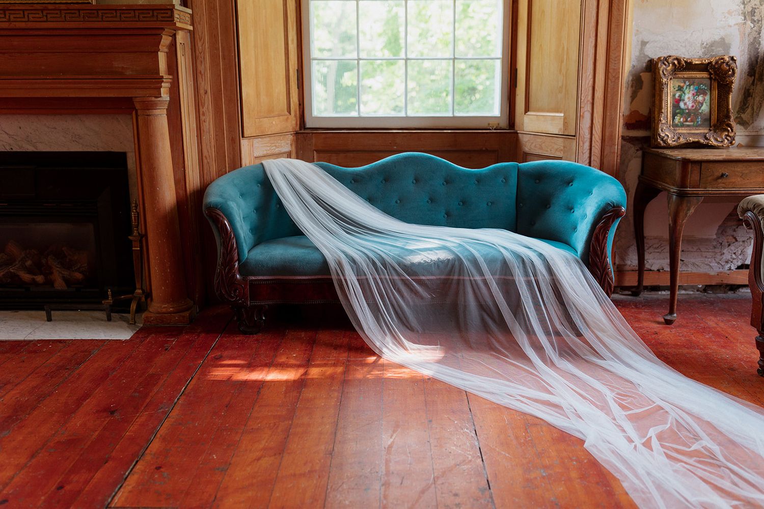 A series of sunlit windows in a historic room with blue velvet furniture and hardwood floors.