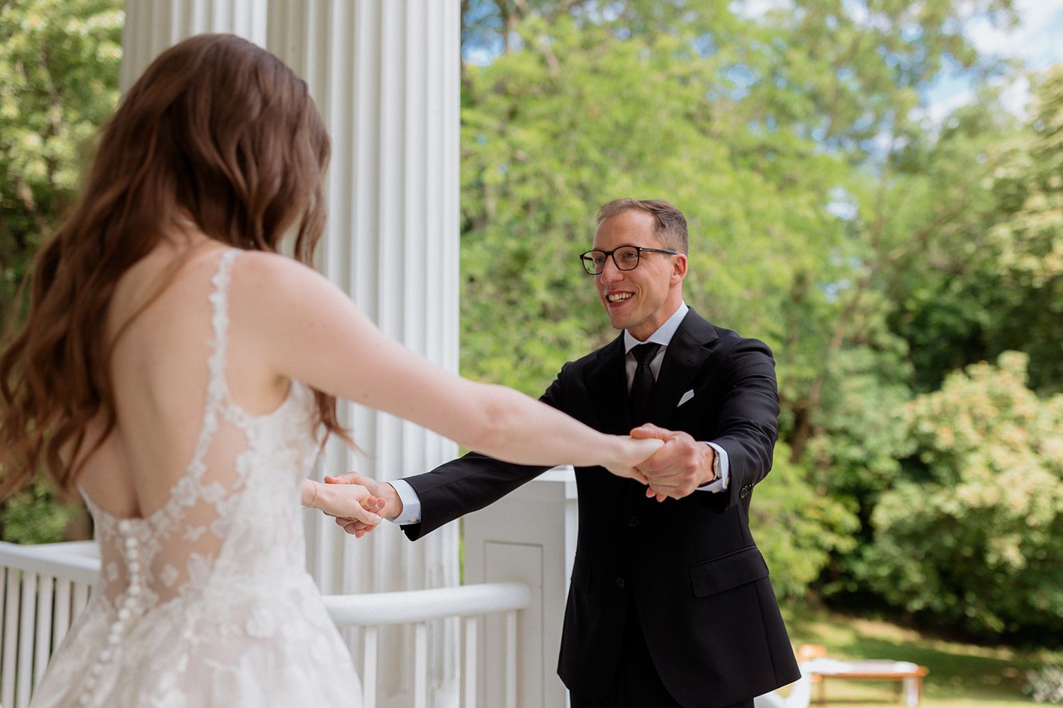 A romantic wedding photoshoot on a white columned porch surrounded by greenery.