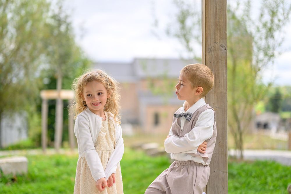 Two young children in white outfits play together outdoors in a grassy area during springtime.