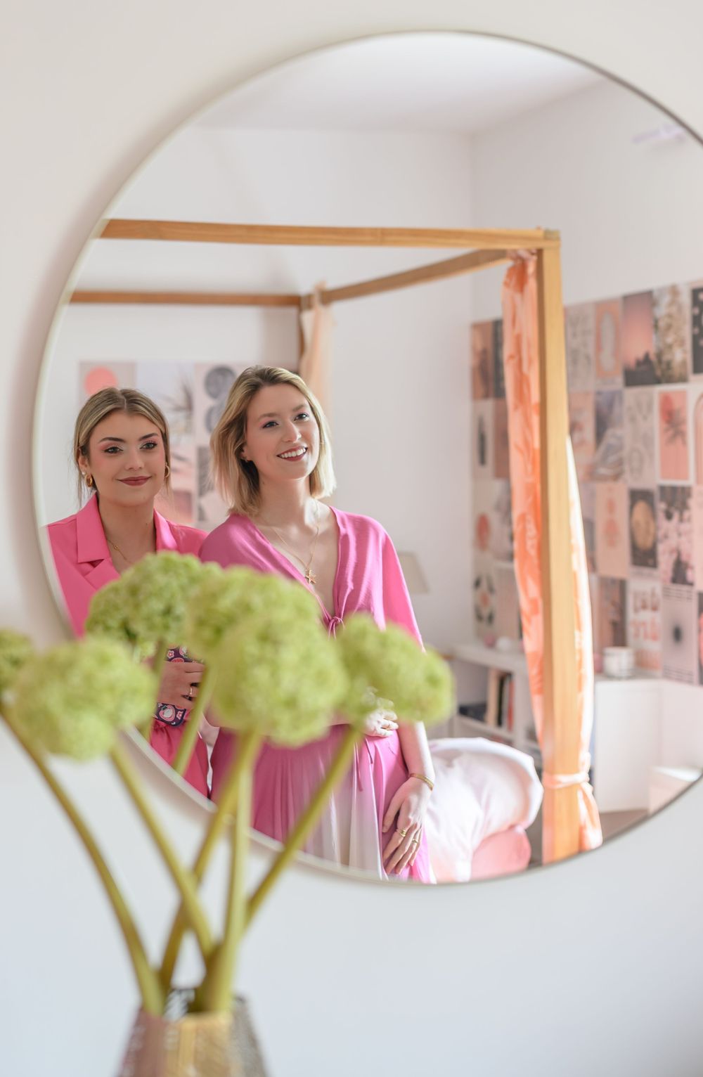 Three round mirrors on a white wall reflect pink clothing and green flowers in a bright interior space.